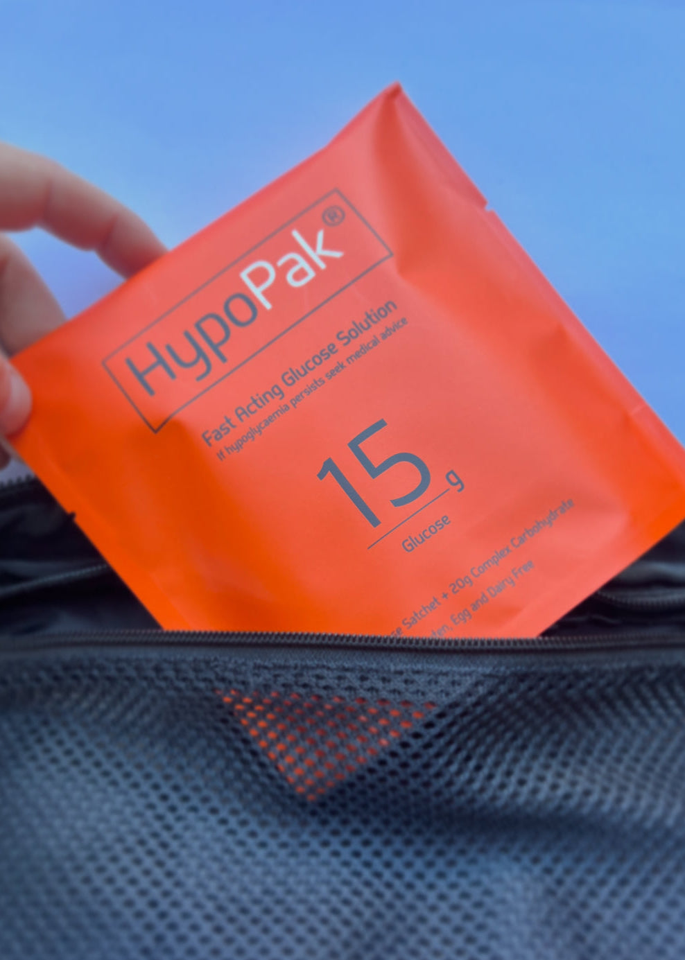 Orange packet labeled 'HypoPak' held over a blue textured surface